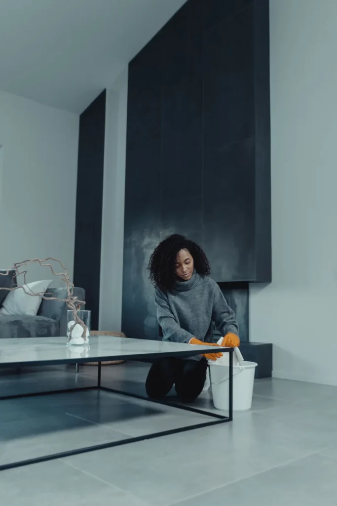 Cleaner kneeling beside a bucket while cleaning a living room