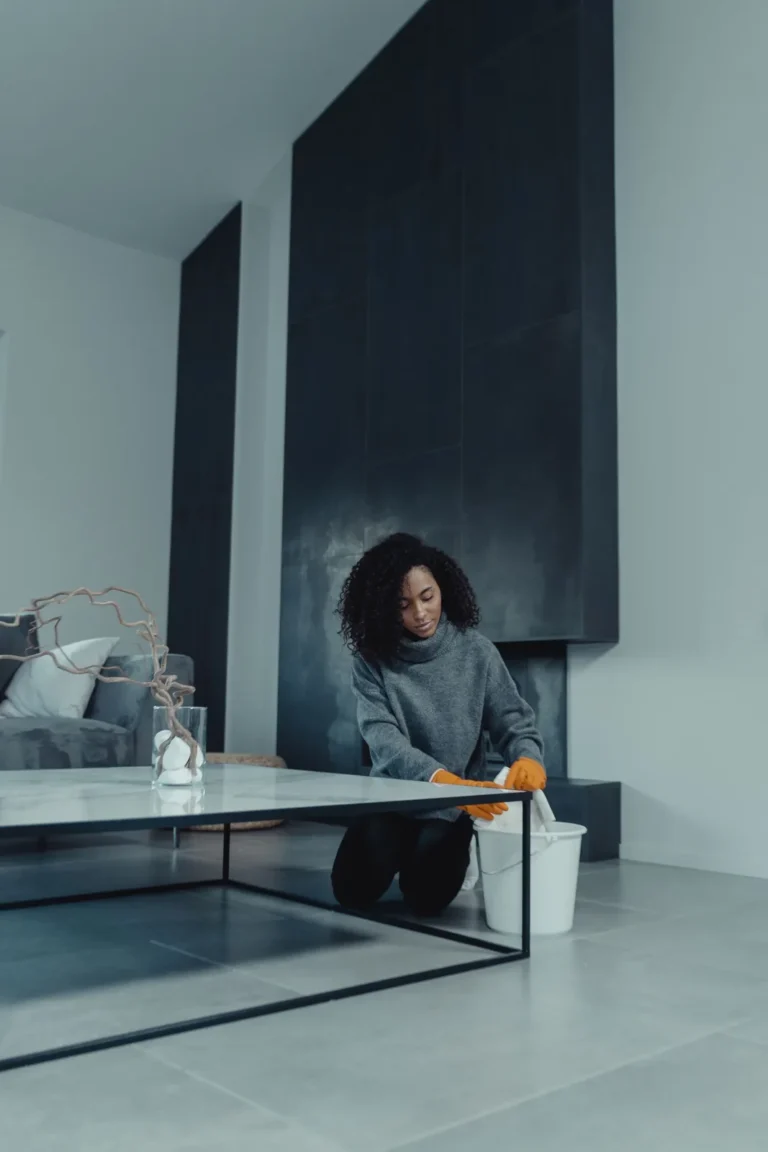 Cleaner kneeling beside a bucket while cleaning a living room