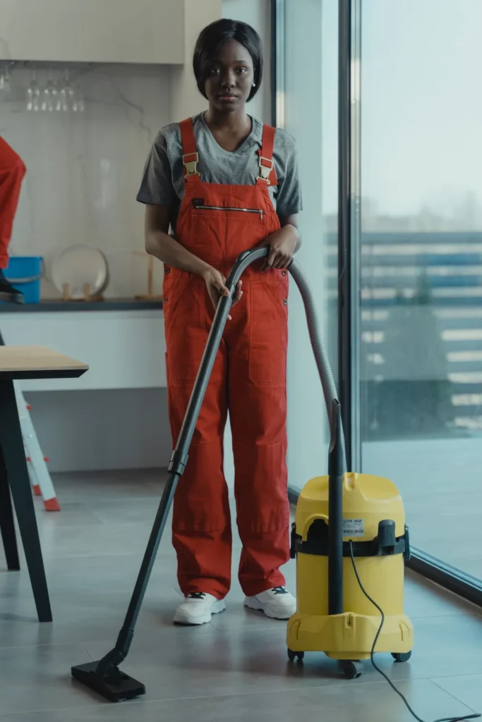 Cleaner in red work overalls vacuuming a bright office